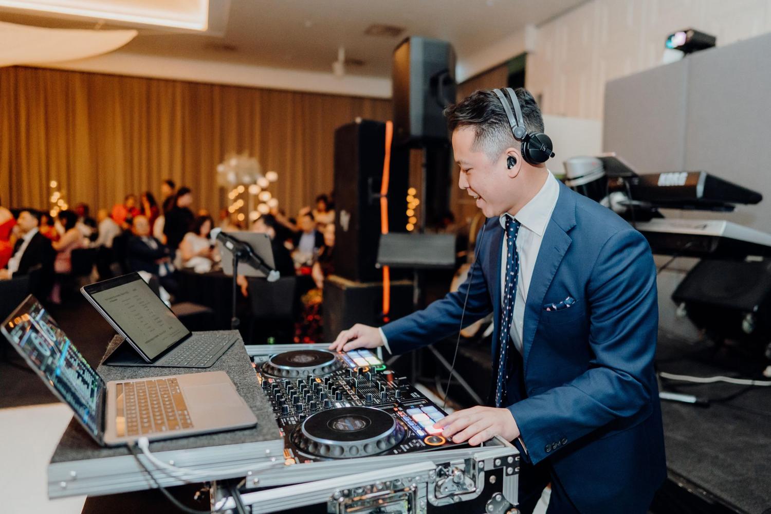 DJ FRNKIIE in a blue suit mixing at a reception
